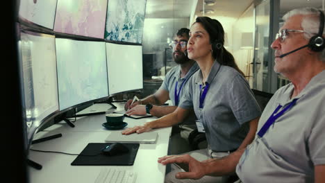 tres personas trabajando en un centro de control, mirando mapas en múltiples monitores.