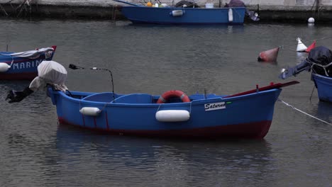 a close shot of a mall blue fishing boat resting in the marina, slowly moving up and down as the waves are approaching