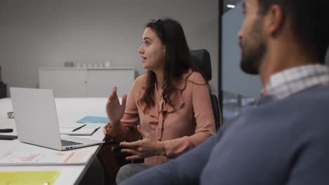 mujer de negocios caucásica sentada con una computadora portátil hablando con un colega masculino en una reunión casual de oficina