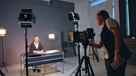 female photographer fixes camera directed on the woman sitting at desk. blog footage in studio.