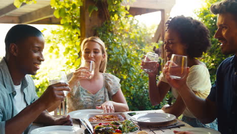 group of smiling multi-cultural friends outdoors at home eating meal and making a toast with water