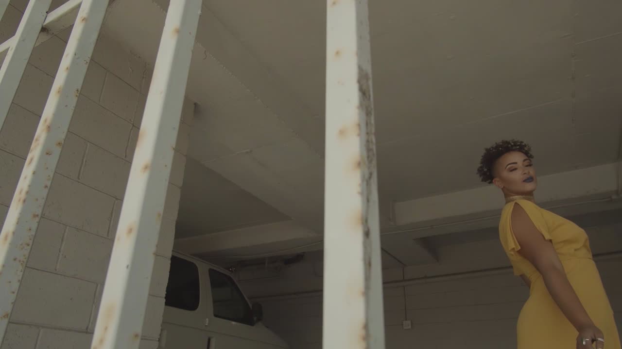 A woman behind the metal grill wearing yellow dress dancing