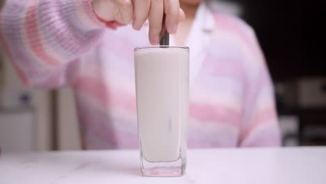 detalle de la mano de la mujer moviendo la leche en una taza de vidrio con un tenedor