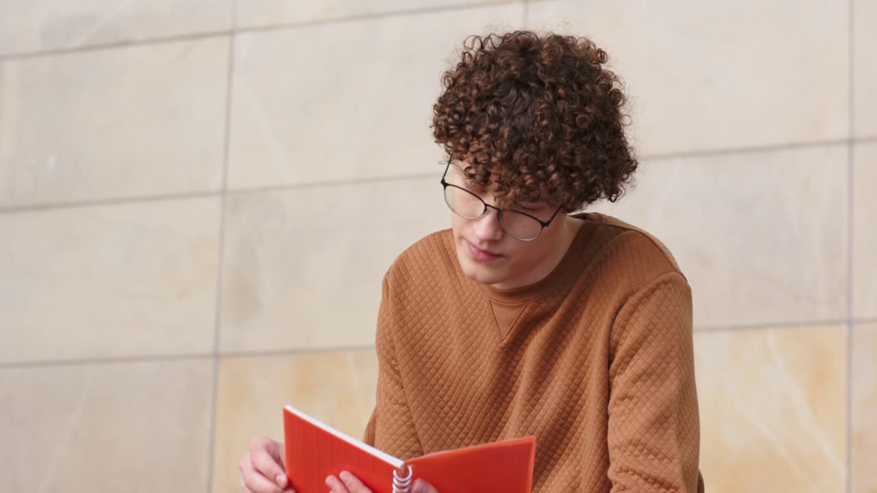 Un homme feuilletant les pages d’un carnet rouge pour trouver des informations, levant les yeux et se concentrant sur un mur carrelé