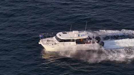 a commercial fishing charter boat cruises rapidly across open ocean waters off the gold coast, australia, captured in golden hour light by a moving drone