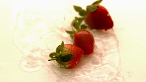 strawberries falling on white wet surface