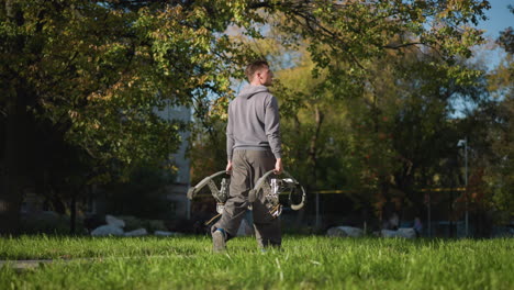 joven caminando en un parque cubierto de hierba con una sudadera gris claro y pantalones gris oscuro, rodeado de exuberante vegetación y árboles, creando un paisaje natural pacífico bajo una luz suave