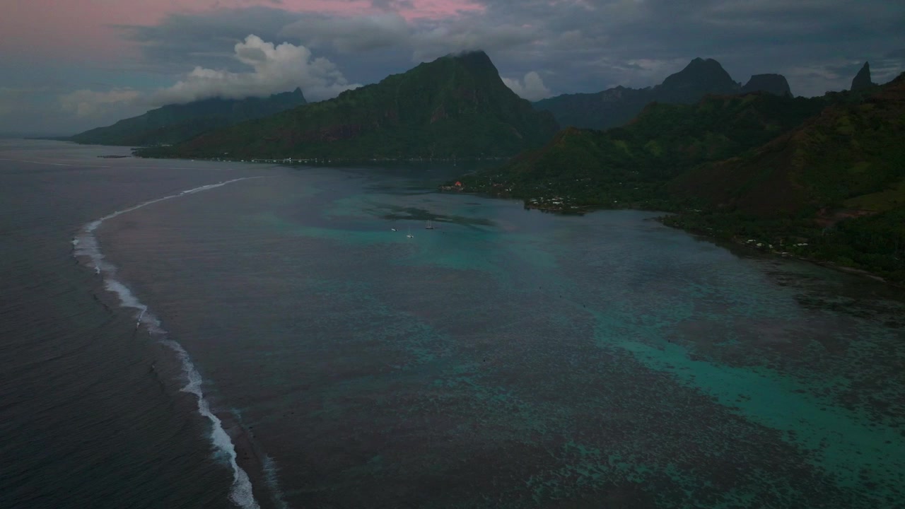 Purple sunset dusk Mount Mauaroa Tohivea Rotui Haapiti Cooks Opunohu Bay Moorea island French Polynesia aerial drone jagged mountains boats lagoon coral reef waves Pacific Ocean forward pan up motion