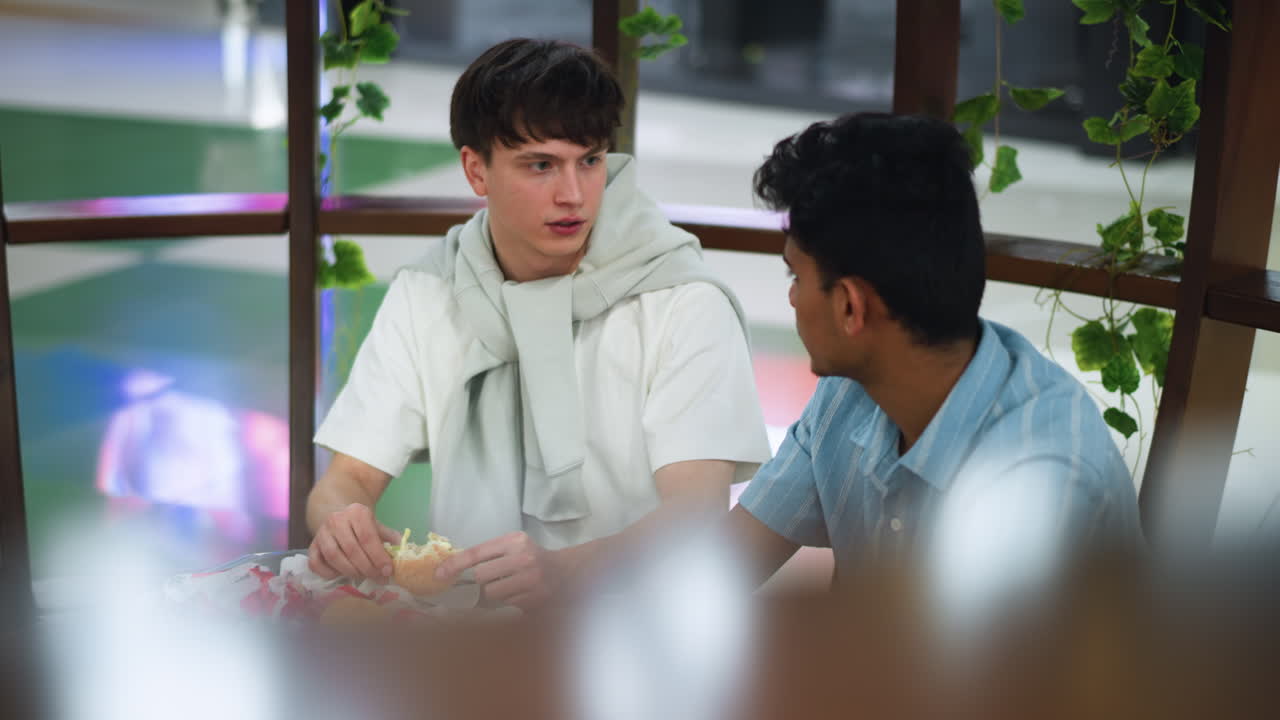 Back view of Indian man with fluffy black hair turning slightly interacting with his friend while sitting in blurred interior, focus on texture and volume of hair creating casual candid mood