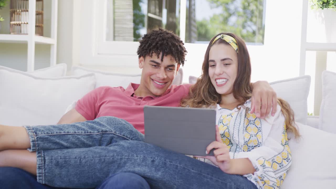 pareja biracial feliz pasando tiempo en casa juntos usando computadora portátil y teléfono inteligente