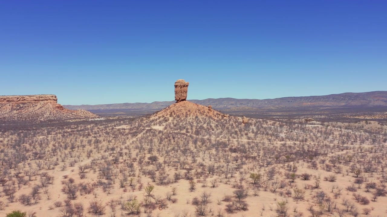 Namibya'daki Fingerklippe kaya iğnesinin drone panoraması. Kuru araziden yükselen devasa oluşum. Çorak, yapraksız ağaçlar ve berrak, bulutsuz öğle gökyüzü görüntüleri.
