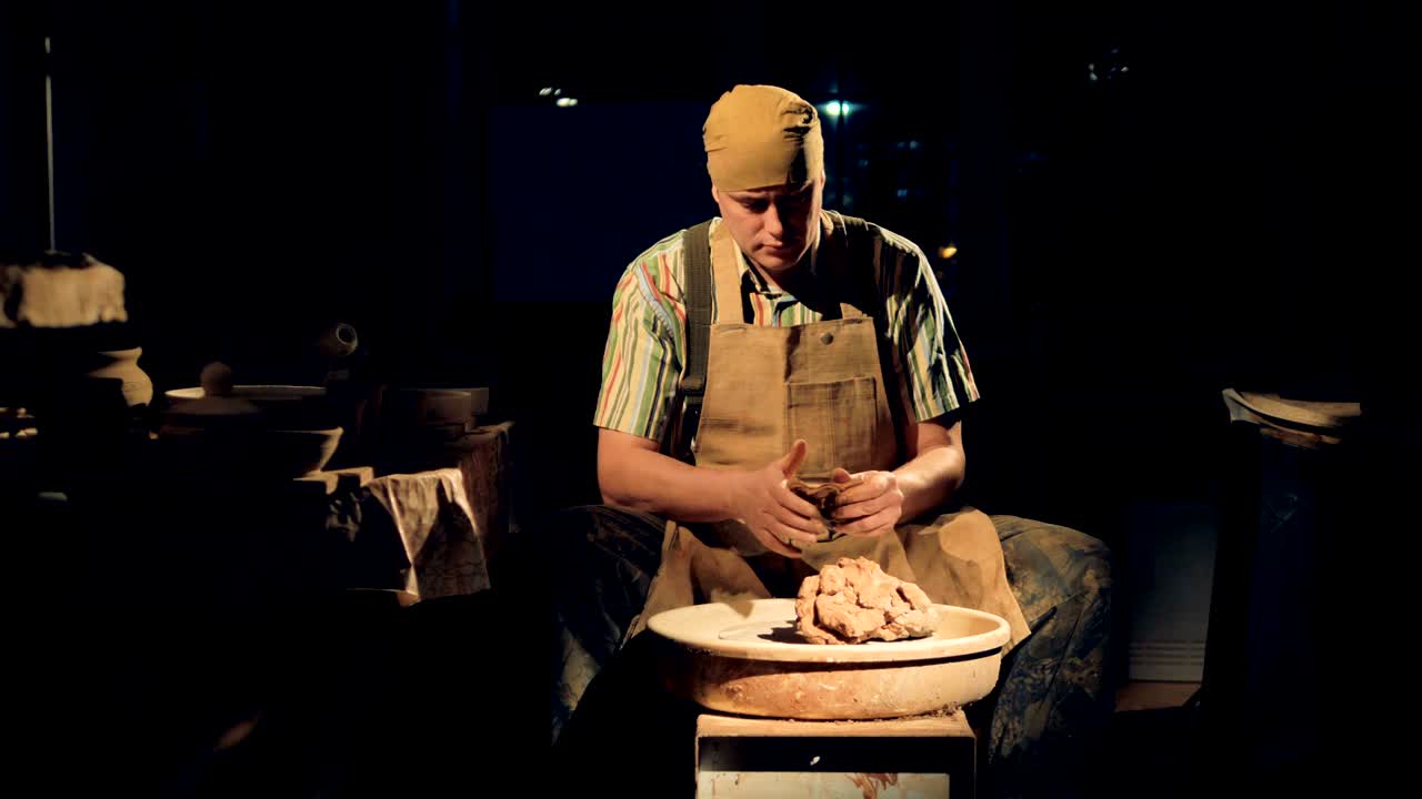 un alfarero en una habitación oscura amasa arcilla.