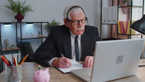 Un-Hombre-De-Negocios-De-Alto-Nivel-Usa-Auriculares-Inalámbricos-Haciendo-Videollamadas-De-Conferencia-En-Una-Computadora-Portátil,-Agente-Del-Centro-De-Llamadas