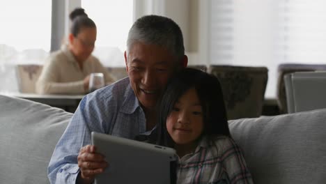 Front-view-of-cute-asian-granddaughter-and-old-senior-grandfather-using-digital-tablet-at-home-4k