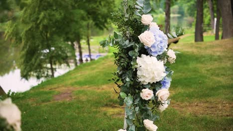 revealing shot of blue and white wedding ceremony flowers on a metal stand with green leaves in the nature near the lake