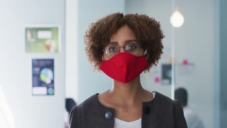 Portrait-of-african-american-woman-adjusting-her-face-mask-at-modern-office