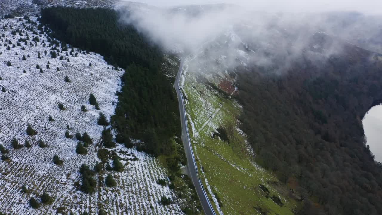tranquilidad invernal: vista aérea de un camino de montaña wicklow vacío dividido por la nieve, envuelto en nubes bajas, revelando la belleza serena de los bosques y el lago guinness
