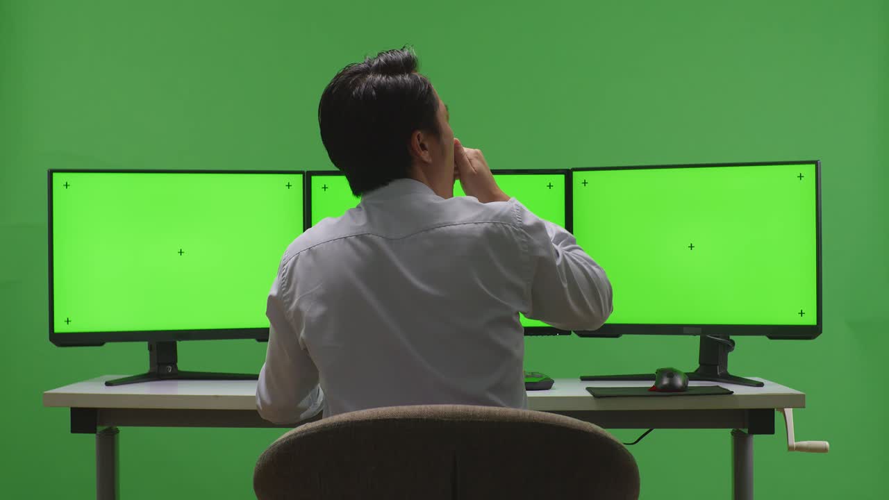 트리플 모니터와 함께 책상에 기대어 있는 사람