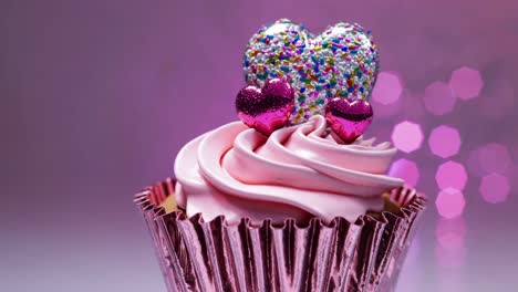 cupcake with pink icing and heart shaped decorations rotates slowly against a backdrop of colorful bokeh, creating a sweet and romantic atmosphere