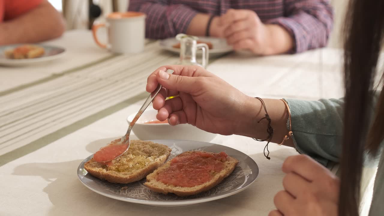 Unrecognizable woman spreading tomato on the bread sitting on a table