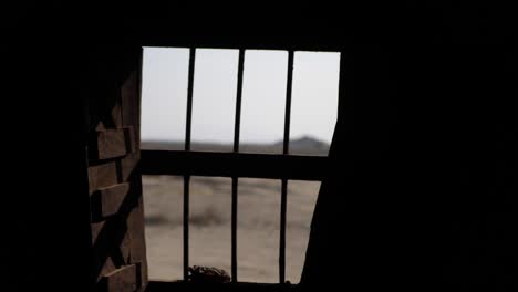 inside dark room looking through metal bars of window out towards arid rural landscape in gwadar