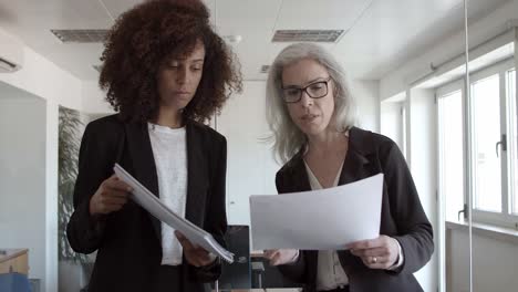 mujeres de negocios con documentos de pie y hablando en la oficina