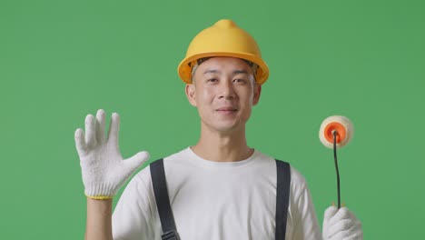 close up of asian man painter wearing safety helmet smiling and saying wow while standing in the green screen background studio
