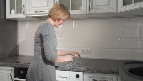 young adult in checkered gown playfully moving cup on kitchen countertop, engaging in fun game, electric outlet visible on wall, lively and casual atmosphere with playful energy