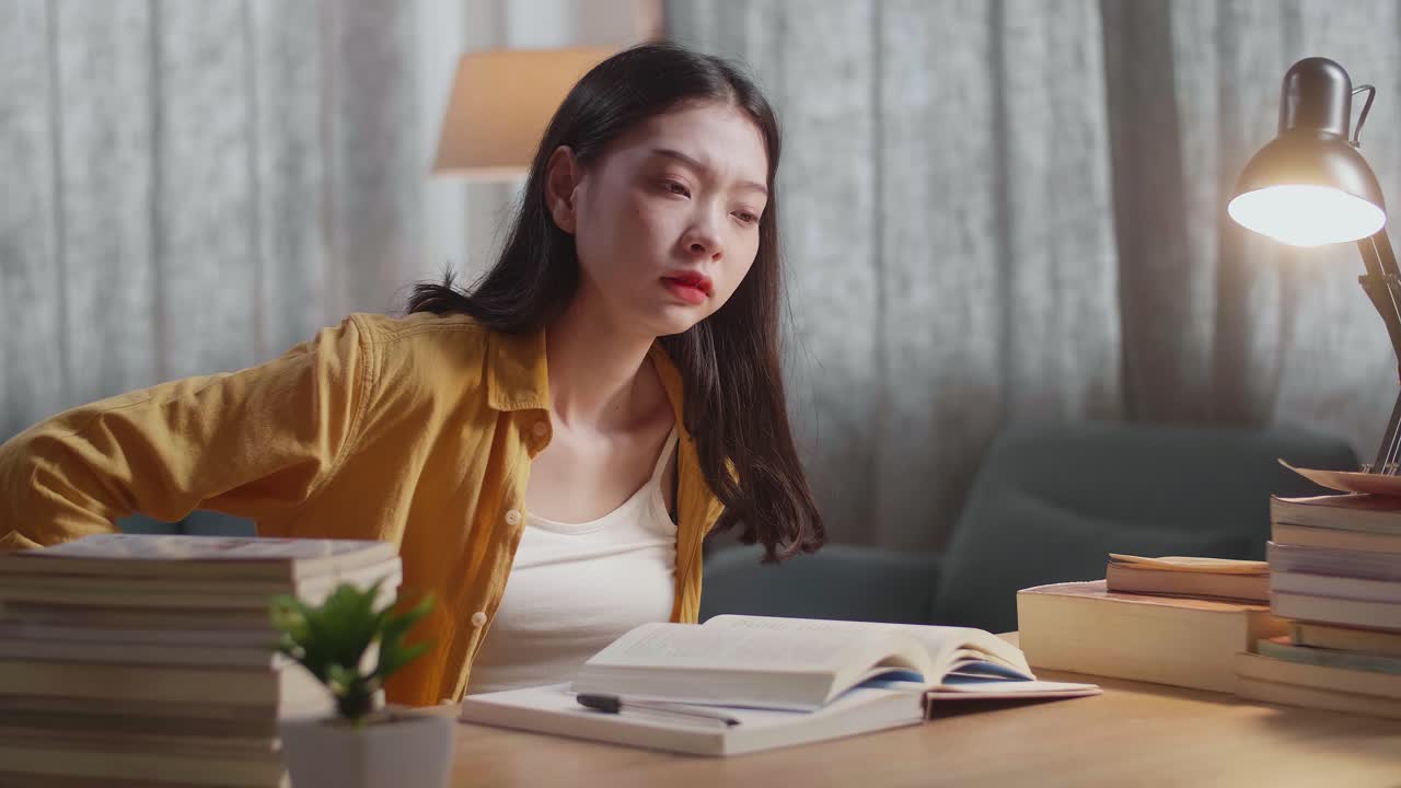 집 에서 공부 하고 책 을 책상 에 놓고 읽는 동안 등 통증 이 있는 젊은 아시아 여성