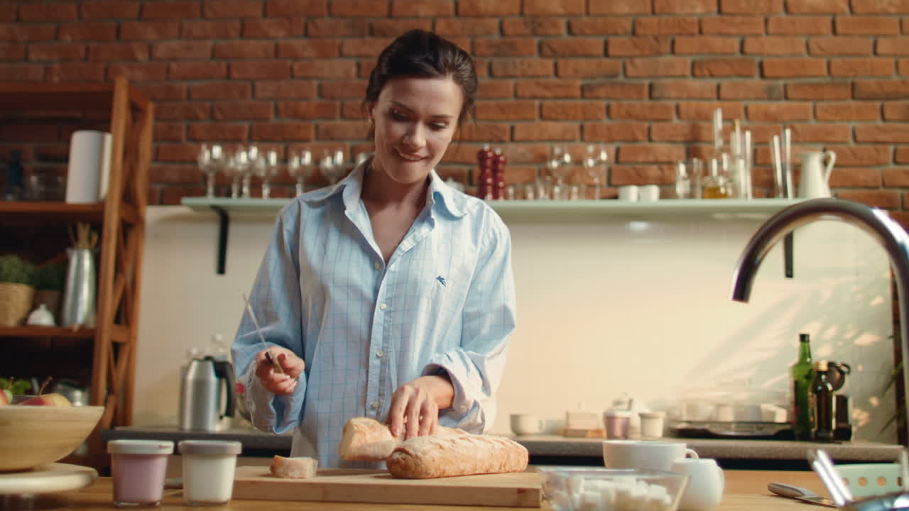 Young woman cutting baguette on wooden board. Girl preparing breakfast at home.