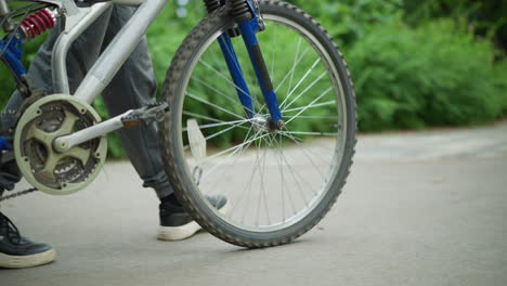 leg view of someone walking closely with his bicycle along a park walkway, with floating shoelaces in motion, the focus is on the legs and bike, with a grassy background and greenery