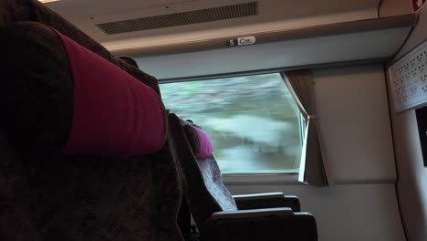 empty first class train seats with pink headrests and forest view through window in japan