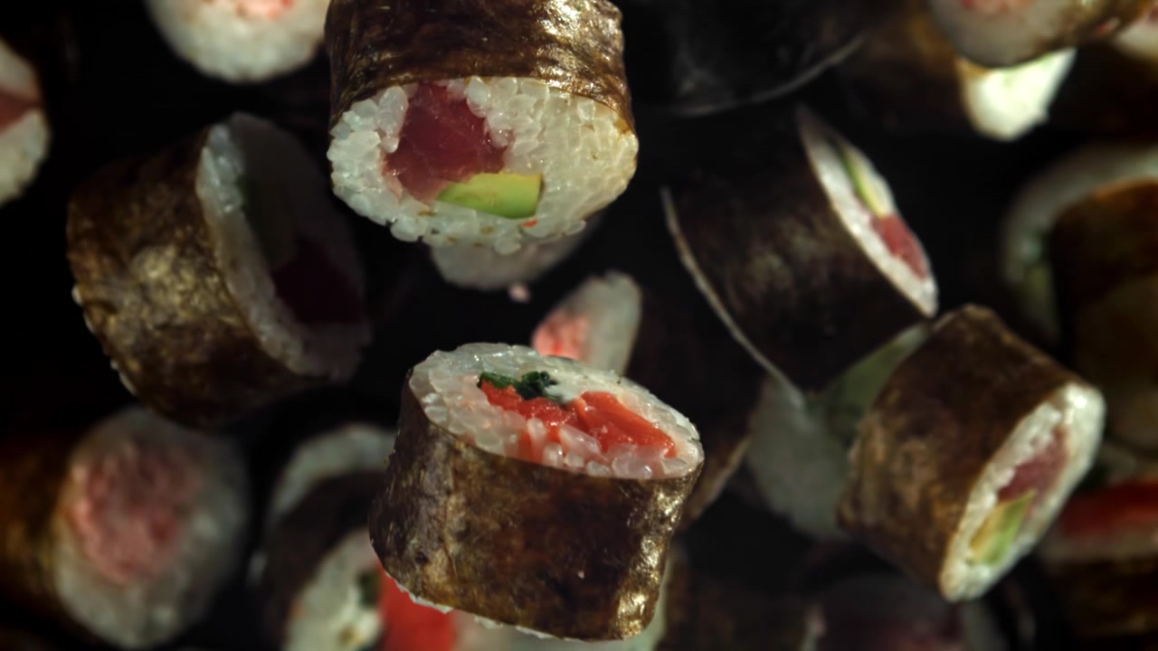 Varietà di roll di sushi che cadono al rallentatore su sfondo nero