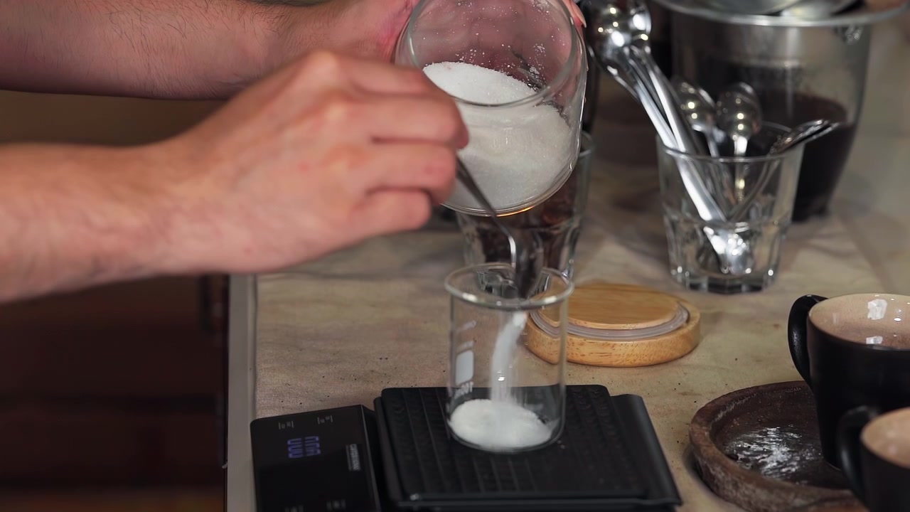 Mano del barista che misura lo zucchero in una tazza di vetro per preparare una bevanda al caffè