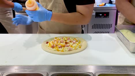 요리사는 준비하는 동안 피자에 소스를 첨가합니다.