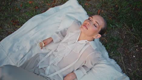 luxury model lying green grass with wine glass top view. chic woman closing eyes