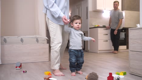 mother helping her baby to take his first steps in the living room at home