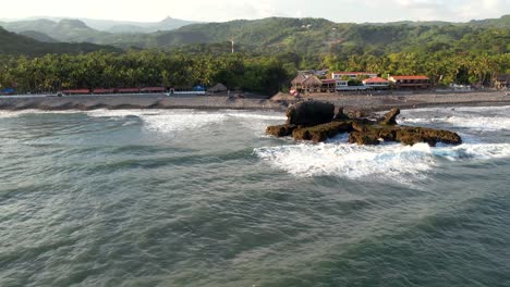 aerial view of waves break on rocks in a blue ocean