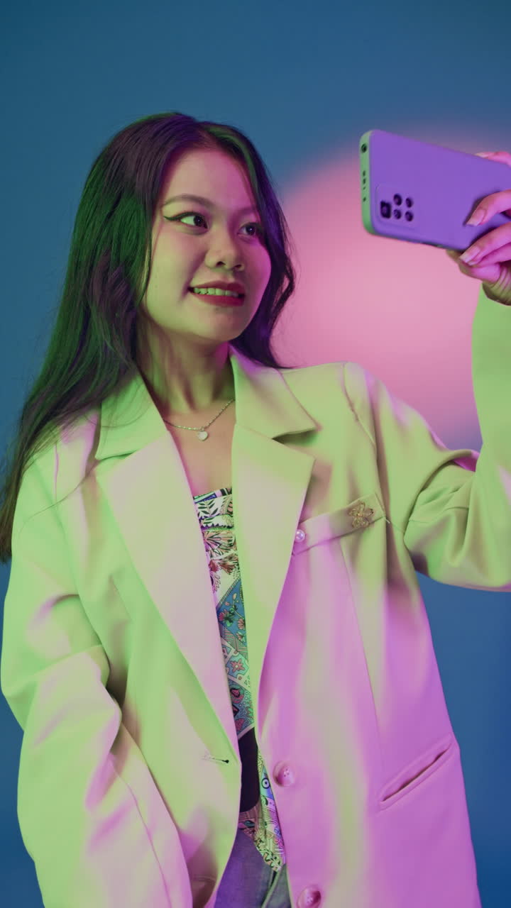 Vertical of Asian Woman Taking Selfies on Phone at Neon Studio