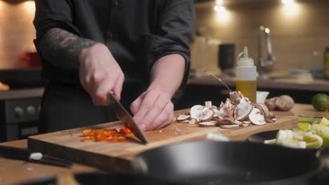 red chili being cut on a wooden board by professional chef in an elegant black shirt with tattoos