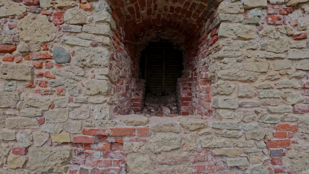 Un'antica parete in pietra e mattoni con un'apertura ad arco riempita di detriti e travi in legno presso il Castello di Bauska in Lettonia, catturata in uno scatto ravvicinato statico.