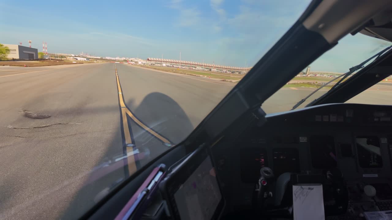 Vista immersiva dalla cabina di pilotaggio di un jet mentre rulla attraverso le vie di rullaggio dell'aeroporto di Madrid, con l'ombra del jet a terra e il Terminal 4 sullo sfondo. Scena illuminata dalla morbida luce dell'alba.
