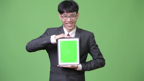 젊은 행복한 아시아 사업가들이 디지털 태블릿을 카메라에 보여주고 있습니다.