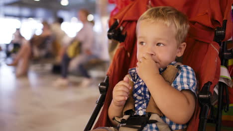 Kleiner-Junge-Sitzt-In-Einem-Kindertrolley-Auf-Einem-Flughafen