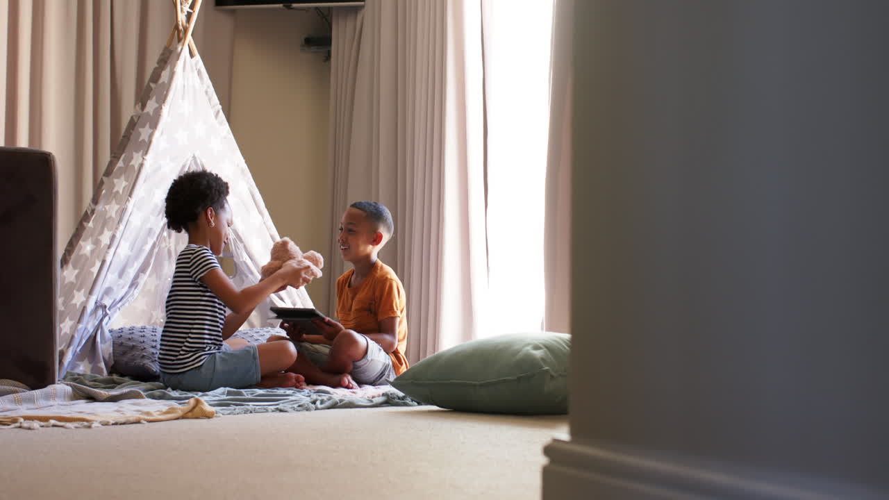 Playing together in living room, children sitting in tent with book and toy
