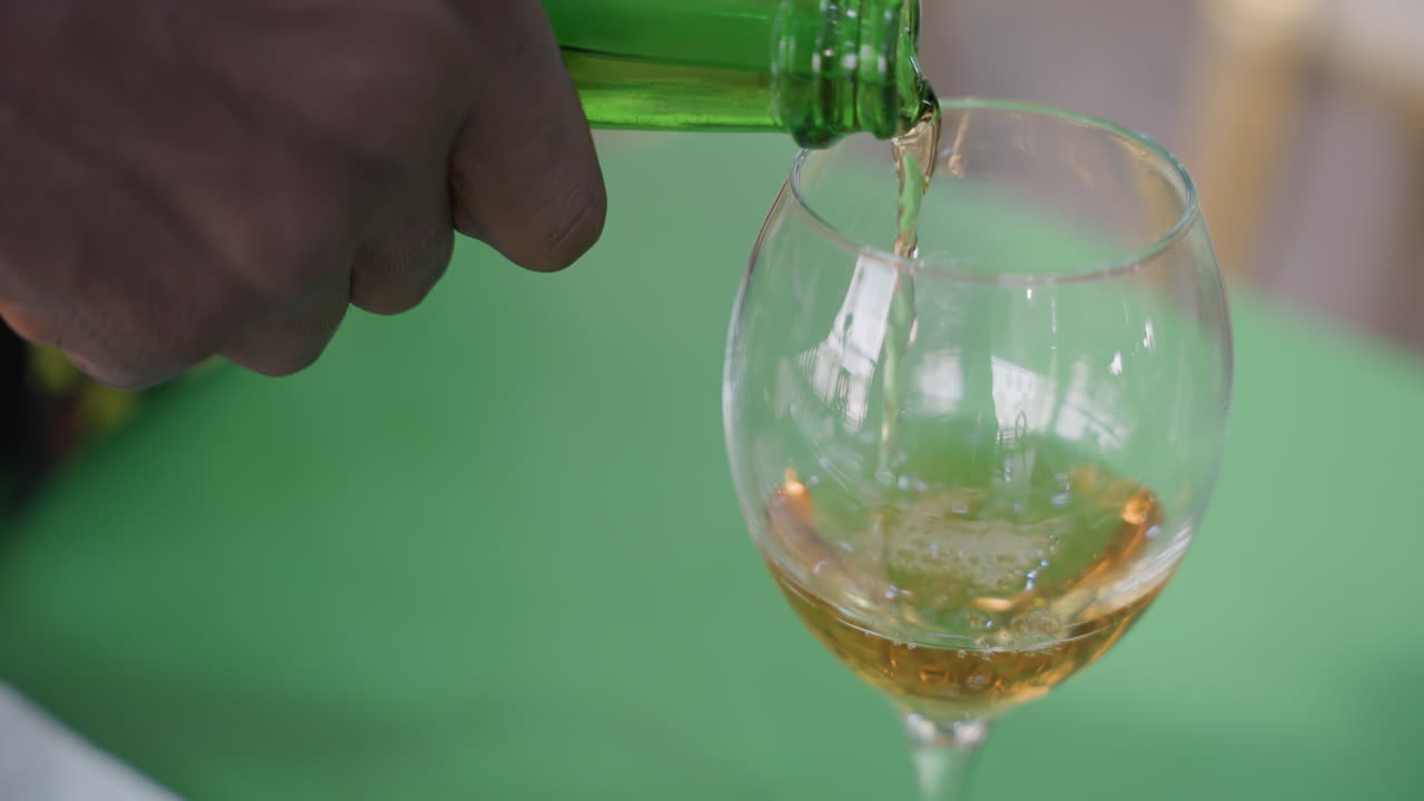 Versare con cura una bevanda ambrata frizzante. Un individuo versa delicatamente vino dorato frizzante su una superficie. Vista ravvicinata di una mano che versa delicatamente vino ambrato frizzante su un tavolo con intimità.
