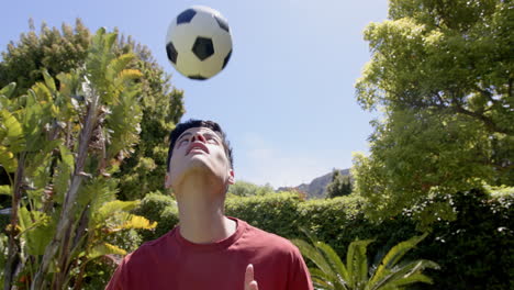 hombre biracial practicando habilidades de fútbol en el jardín soleado, copia espacio, cámara lenta