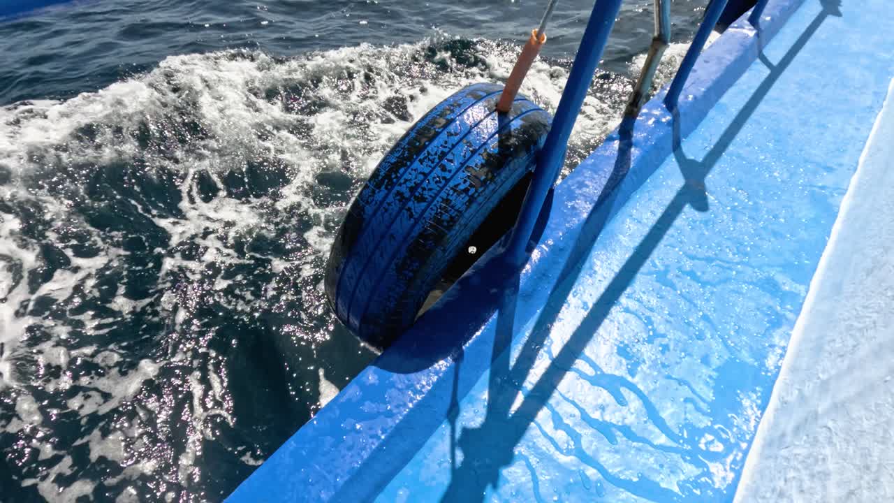 Close-up of blue boat tire fender with sunlit ocean waves, steady camera, vibrant daylight