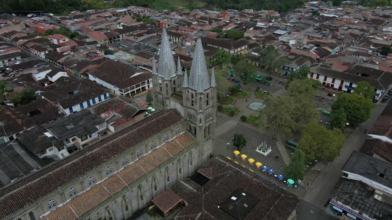 Aerial orbit of Basilica of the Immaculate Conception in Jardin, Colombia, colorful town streets surrounded by lush green hills