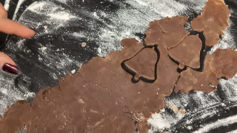 using a cookie cutter to cut bell-shaped gingerbread christmas cookies